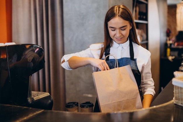 段ボールのカップでコーヒーを準備するコーヒーショップでバリスタの女性