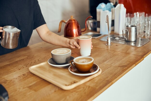 Barista woman making cappuccino here in cups and to go, female preparing coffee drink. Coffee cup with latte art.