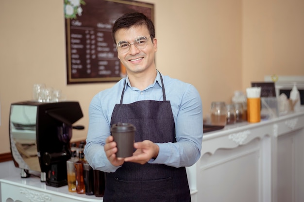 バリスタは、コーヒーショップで顧客に提供するためにホットコーヒーとパン屋のカップを手に取っています