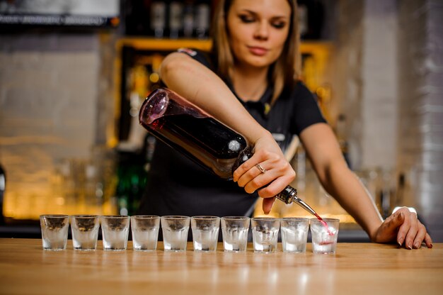 Barmaid pours alcohol into crystal stacks that are lined up