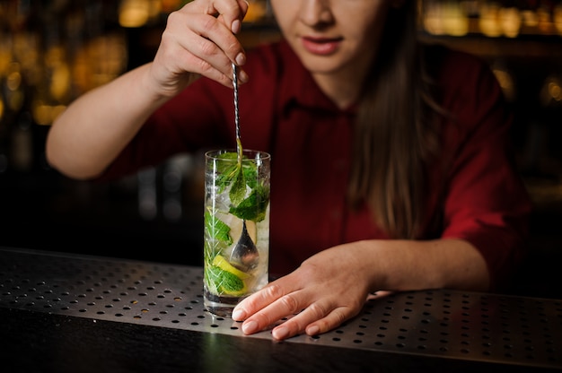 Barmaid with pink manicure mixes an alcoholic cocktail mojito with a spoon