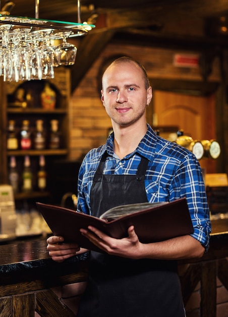 Barman aan het werk in pub, Portret van vrolijke barmanarbeider permanent, Ober die menu's geeft, Een pub.Bar.Restaurant.Classic.Evening.Europees restaurant.European bar.American restaurant.American bar.