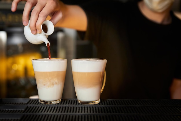 Barman bereidt koffie latte door zwarte koffie in een glazen mok met opgeschuimde melk te gieten