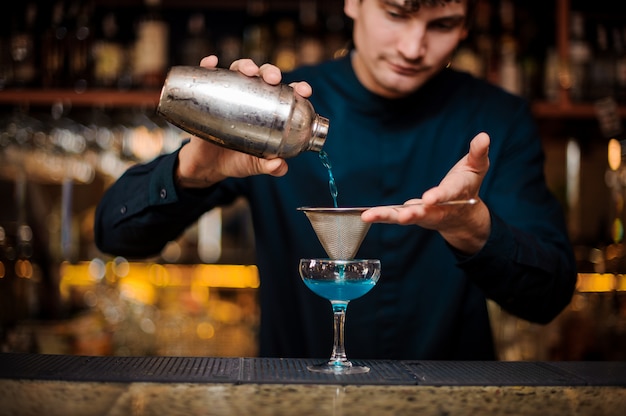 Il barman in una camicia blu filtra un cocktail alcolico blue lagoon