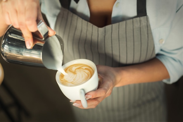 Barman die cappuccino maakt. Close-up van vrouwelijke hand die heet melkschuim giet in espresso. Latte art, klein bedrijf en professioneel koffiebrouwconcept