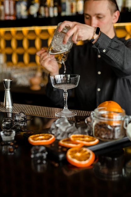 Barman die een alcoholische verse rode luxecocktail uitvoert aan de bar Versierd met sinaasappels