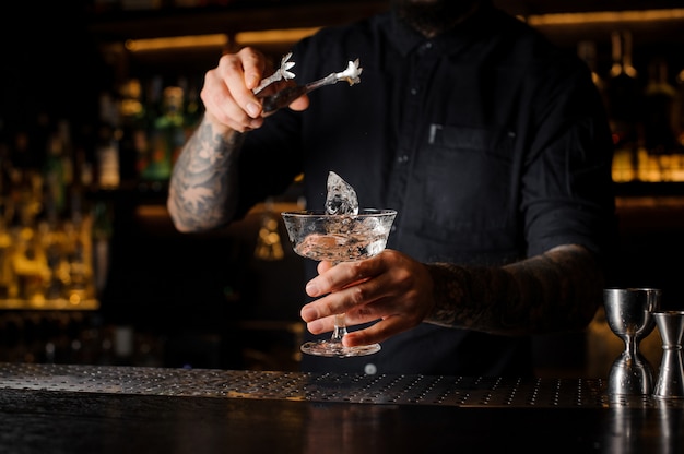 Barman die een ijsblokje in een cocktailglas zet