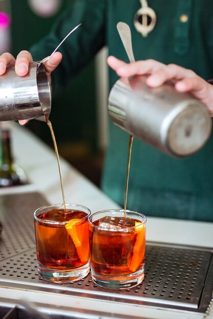 Barman die een negroni-cocktail maakt aan de bar: een drankje uit een shaker in een glas gieten