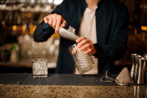 Barman die ijsblokjes in een leeg glas zetten