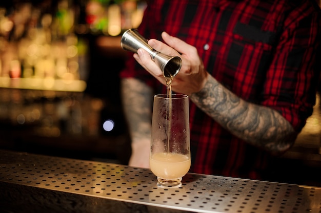 Barman een portie alcoholische drank met jigger gieten in een cocktailglas op de bar