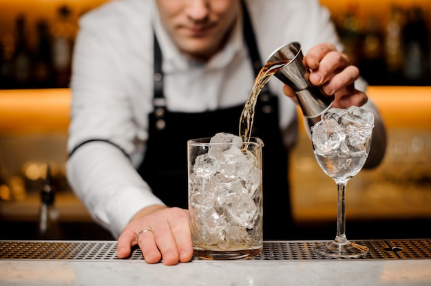 Barman gekleed in een wit shirt gieten alcoholische drank in een glas met ijsblokjes