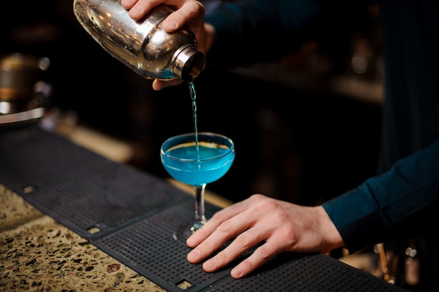 Barman giet een blue lagoon-cocktail met alcohol in het glas