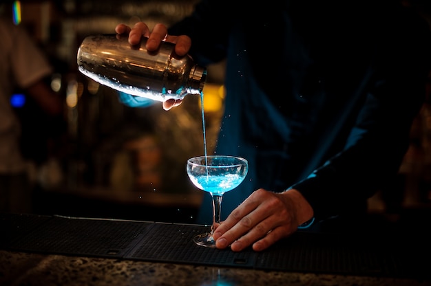 Barman giet van een shaker in een glas alcoholcocktail Blue Lagoon