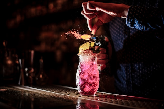 Foto mano del barista che produce un cocktail estivo dolce e fresco di mojito alla fragola con una nota del fumo sui precedenti scuri