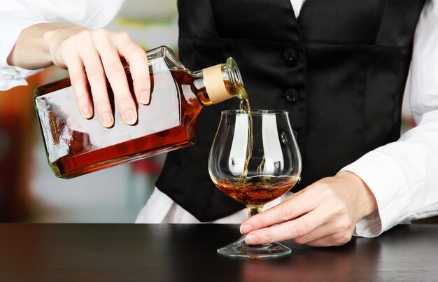 Barman hand met fles cognac drank gieten in glas op lichte achtergrond