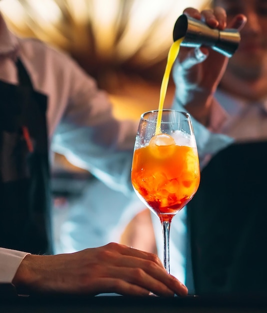 Mano del barista che mescola un cocktail estivo fresco e dolce all'arancia con un cucchiaio sul bancone del bar.