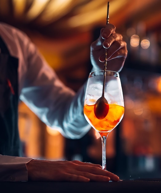 Barman hand stirring a fresh and sweet orange summer cocktail with a spoon on the bar counter.