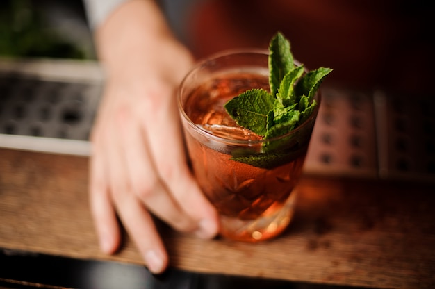 Barman holds a cocktail with mint in his hand