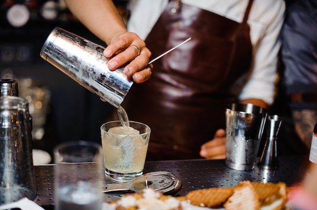 Barman in een bruin lederen schort gieten cocktail in het glas