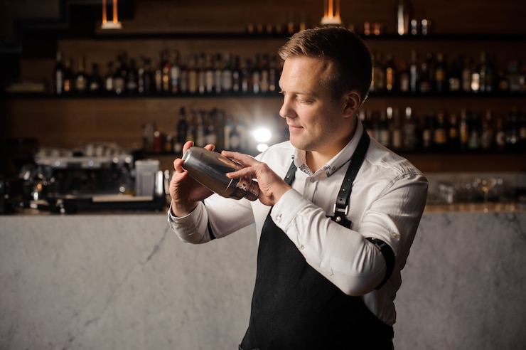 Foto barman in een wit shirt en schort met een shaker tegen de toog