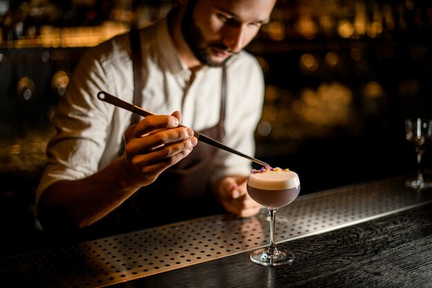 Barman in schort versierd uitschot van de lichtviolette kleurcocktail met gele en paarse bloemblaadjes