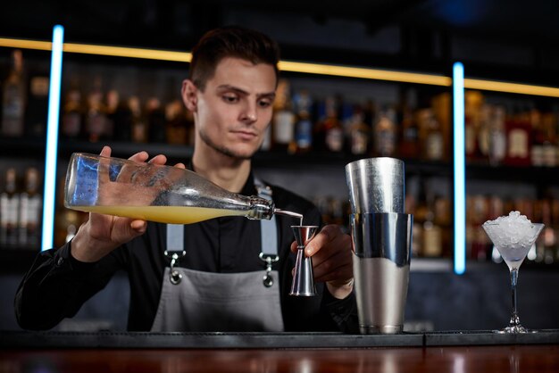 Barman in schort voegt ingrediënt toe aan shaker