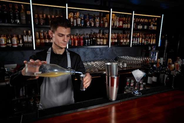 Barman in schort voegt ingrediënt toe aan shaker