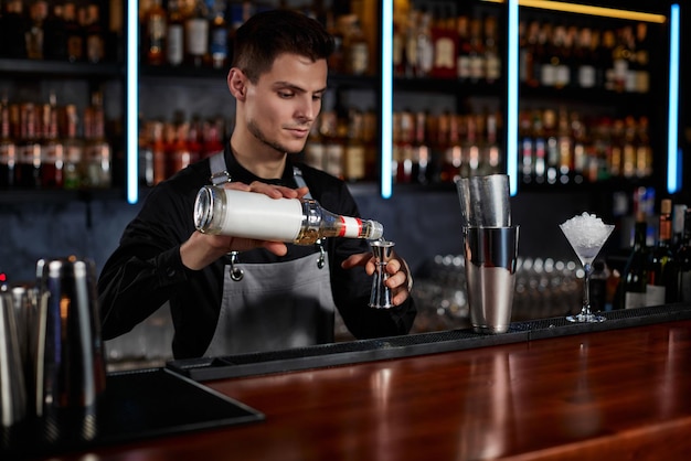 Barman in schort voegt ingrediënt toe aan shaker