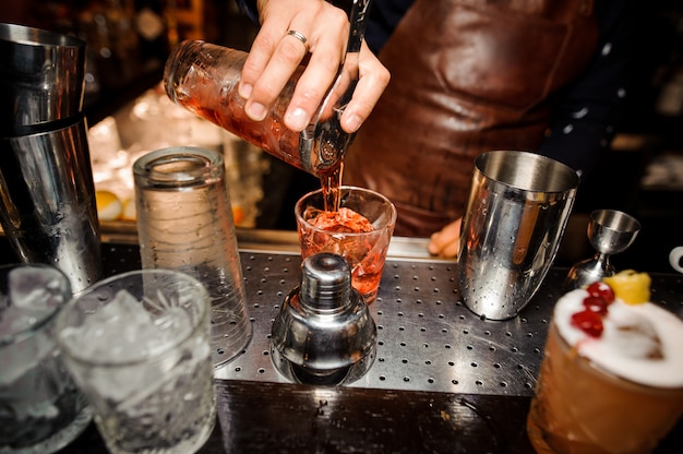 Photo barman is pouring out of a shaker into a crystal glass an alcoholic cocktail