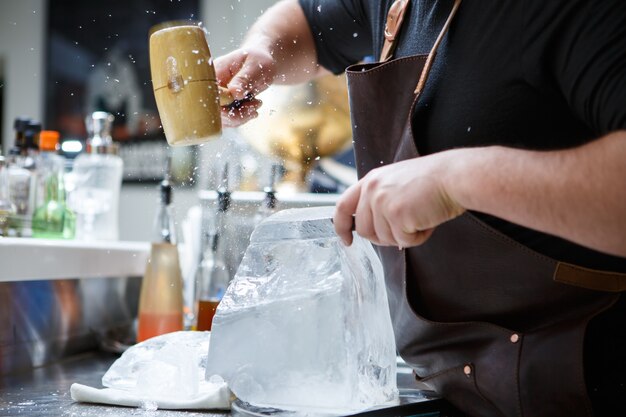 Barman maalt manueel ijs met houten hamer en metalen mes.