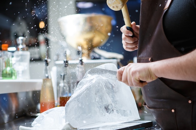 Barman maalt manueel ijs met houten hamer en metalen mes.