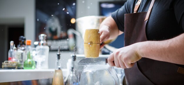 Barman maalt manueel ijs met houten hamer en metalen mes.