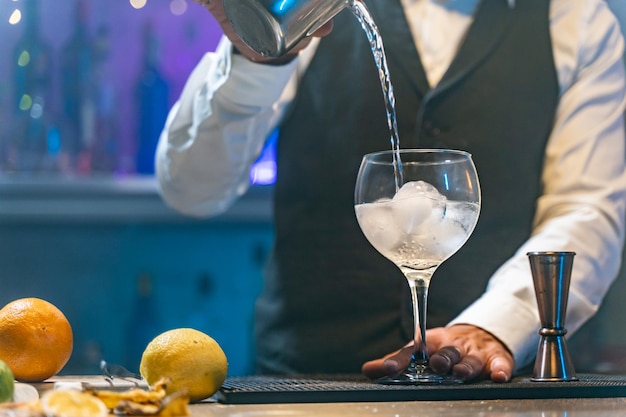 Бармен готовит коктейль в ночном клубе, добавляя ингредиенты и создавая опытные напитки на барной стойке