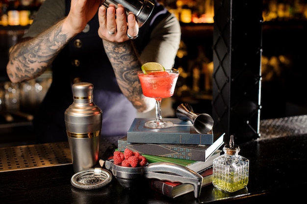 Barman making fresh and sweet red sweet summer cocktail arranged on books