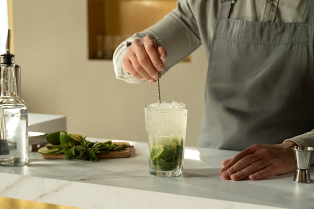 Barman mengt een alcoholische mojito-cocktail met een lepel