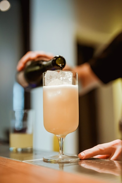 Barman mousserende wijn gieten in een cocktailglas met pina colada. Foto met ondiepe scherptediepte. Verticaal levensstijlbeeld.