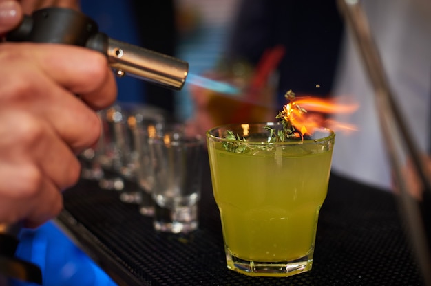 Barman prepares cocktail with orange and herbs in transparent glass