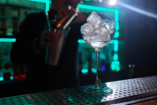 Barman in shirt and apron making an alcoholic drink with ice in a cocktail glass