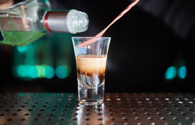 Barman in shirt and apron making an alcoholic drink with ice in a cocktail glass