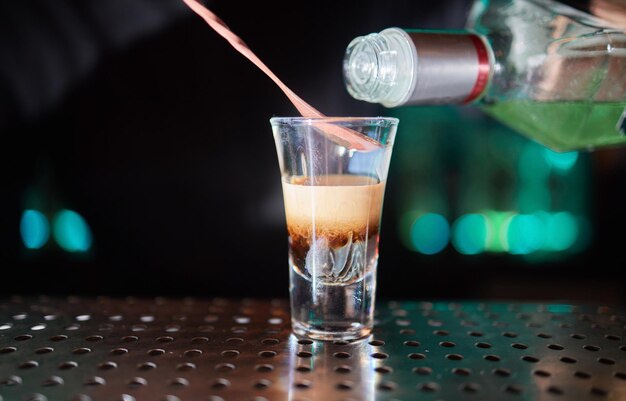 Barman in shirt and apron making an alcoholic drink with ice in a cocktail glass