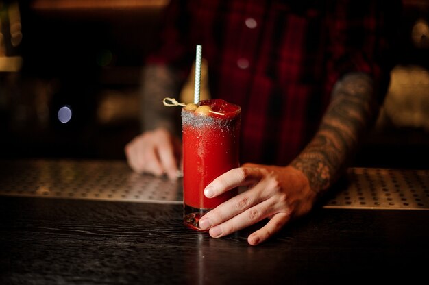 Barman with a glass of salty red tomato bloody mary cocktail decorated with salt and olives with staw