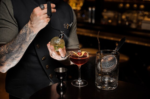 Barman with tattoo making a fresh and sweet summer cocktail with cherries and liquor