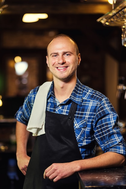 Barman at work in pub,Portrait of cheerful barman worker standing,Waiter giving menus,A pub.Bar.Restaurant.Classic.Evening.European restaurant.European bar.American restaurant.American bar.