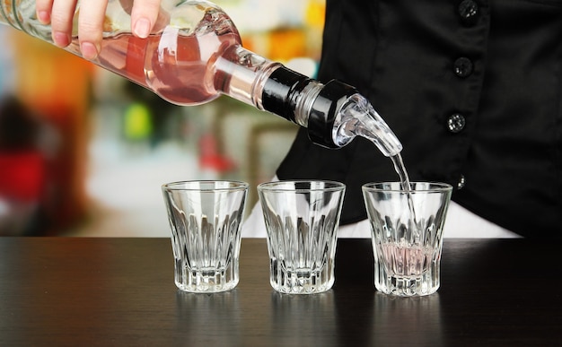 Barmannenhand met fles die drank in glazen gieten, op lichte achtergrond