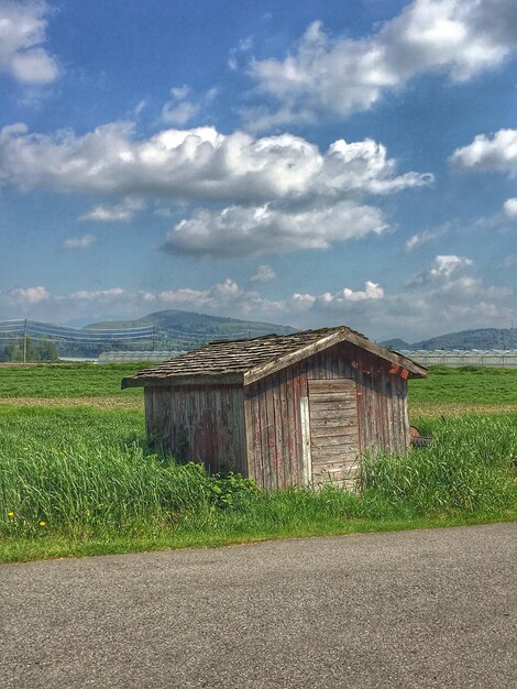 Barn on field by houses against sky