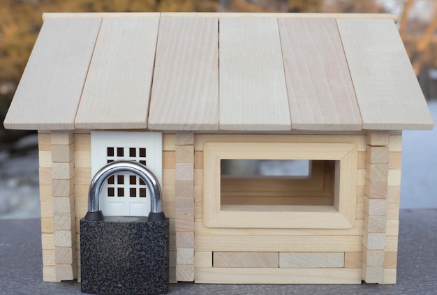 A barn lock stands at the front door of a miniature wooden house. Real estate protection concept.