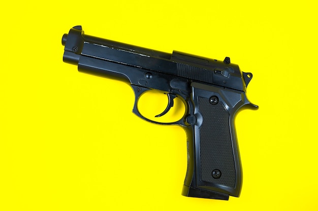 Barrel of a black gun, pistol lies on a yellow background. Close up.