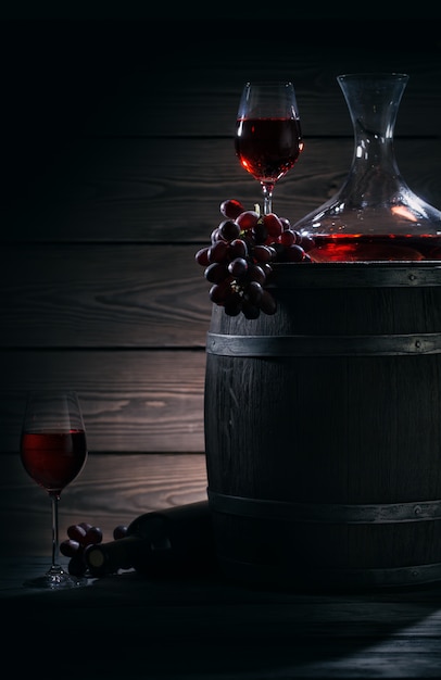 Barrel, decanter and glasses with red wine in a dark cellar