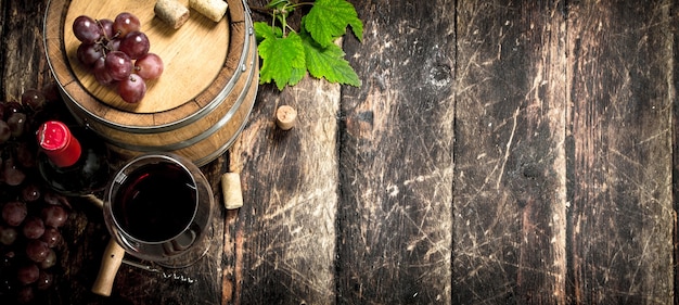 Botte di vino rosso con uva e un cavatappi. su uno sfondo di legno.