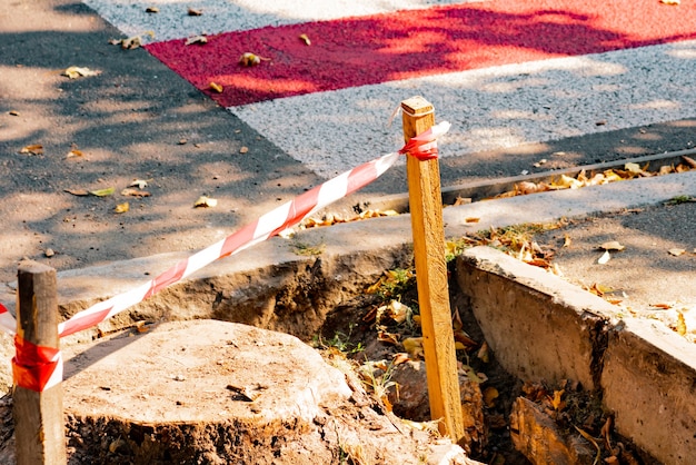 Barrier red and white striped tape on a small wooden pole. Construction site on the sidewalk. Crosswalk for pedestrians. Repair. Works